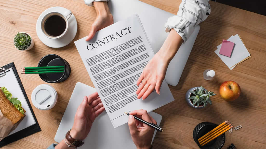 table with assorted items and two people passing a contract back and forth