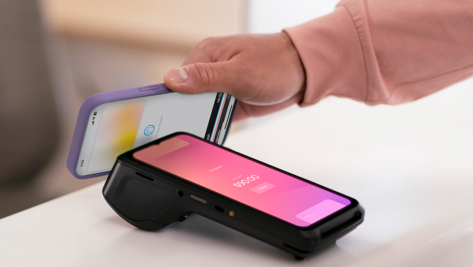 Image of a hand using a phone to make a payment to a card reader with another card reader with a chip inserted